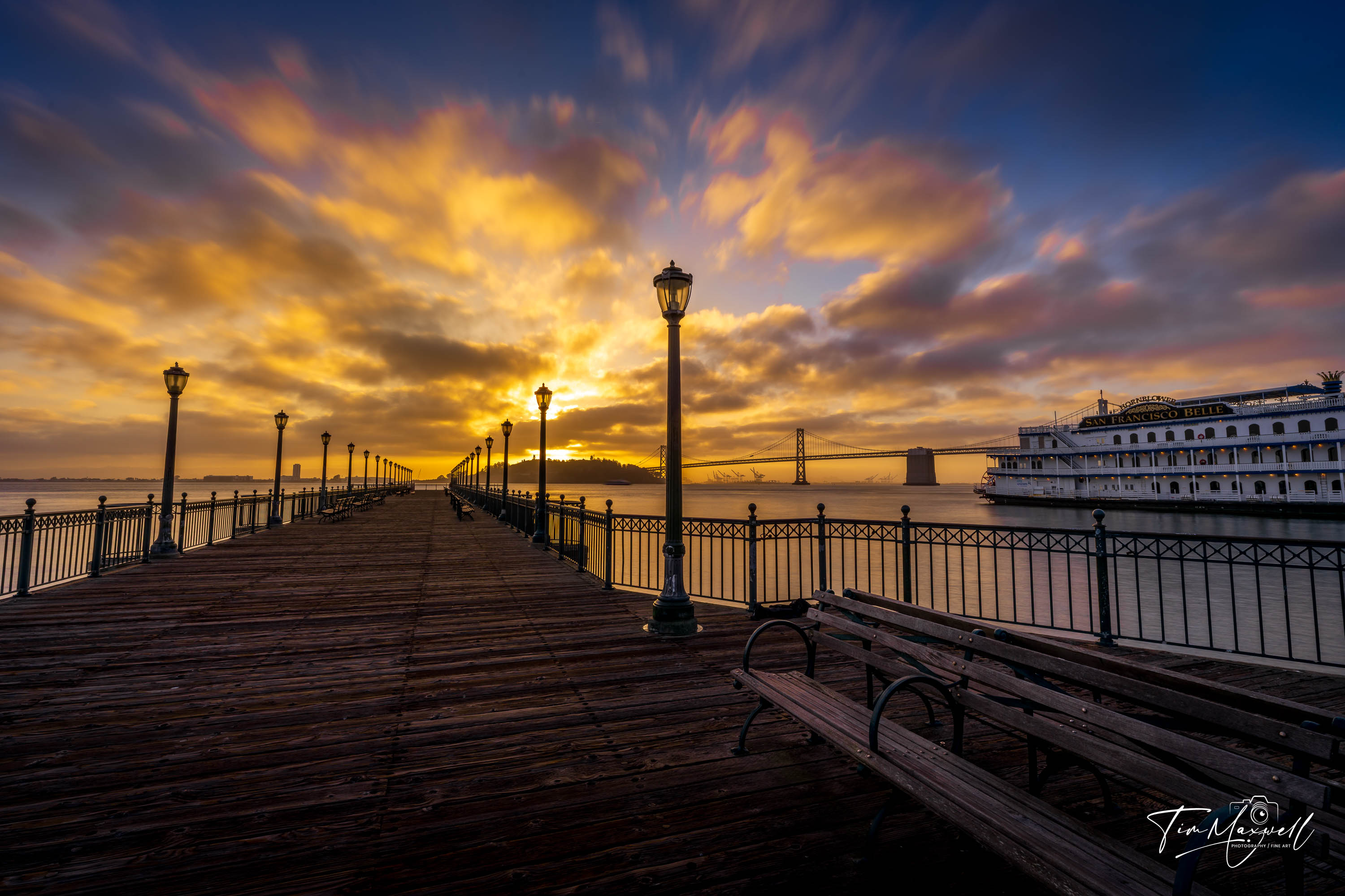 Sunrise over the Bay Bridge with glowing sky and the San Francisco Belle riverboat docked beside Pier 7