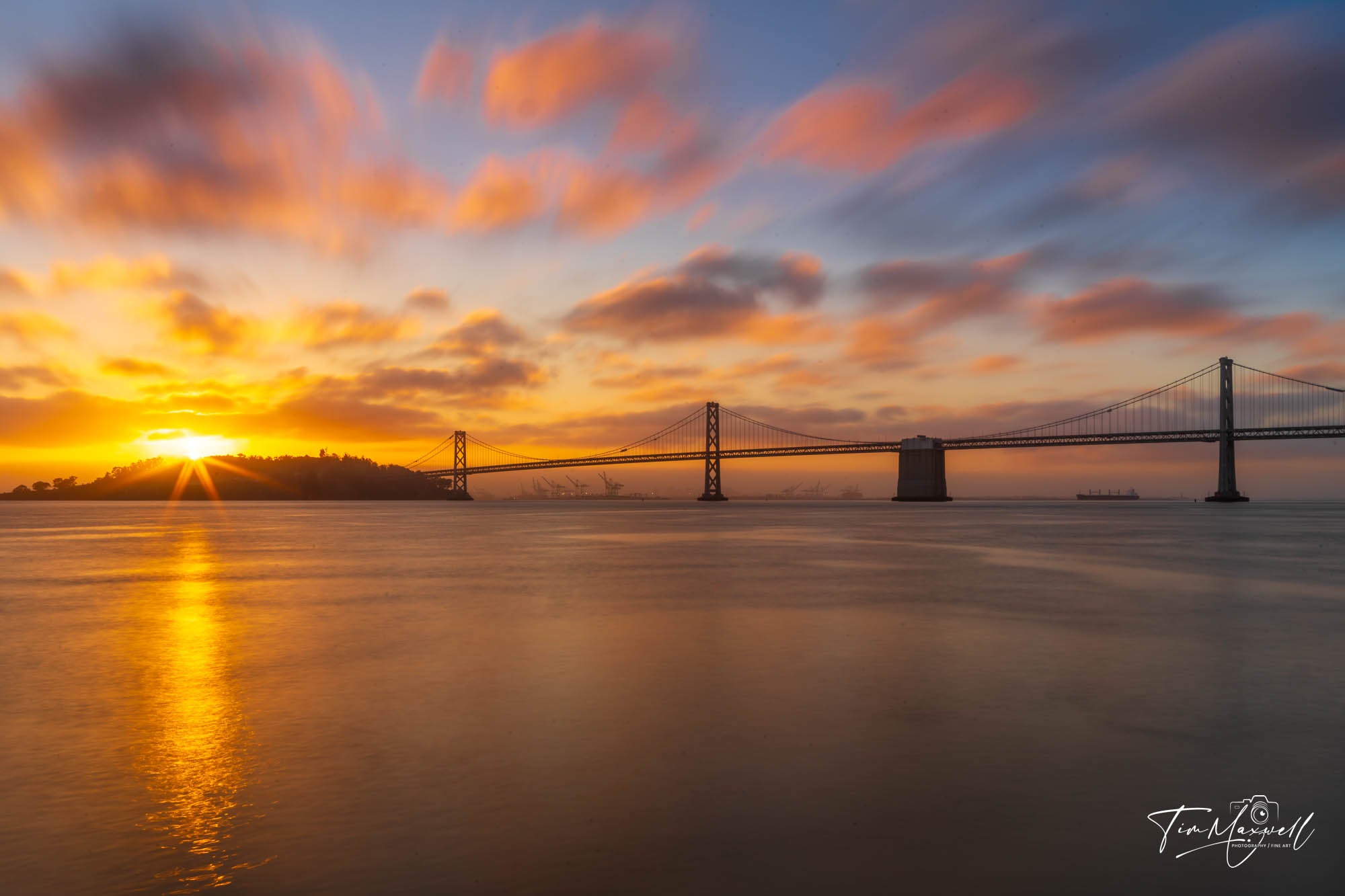 Sunrise behind the Bay Bridge viewed from Pier 7 in San Francisco with golden light reflecting on the bay and streaked clouds in the sky